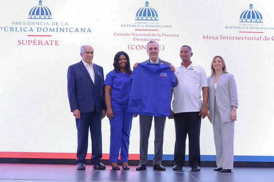 El-presidente-Luis-Abinader-recibe-el-uniforme-simbolico-de-cuidador_-le-acompanan-el-director-ejecutivo-de-Conape-la-directora-general-de-Superate-y-dos-personas-cuidadoras