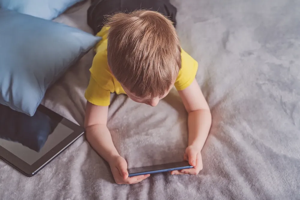 nino-jugando-movil-tablet-tumbado-cama-pantallas